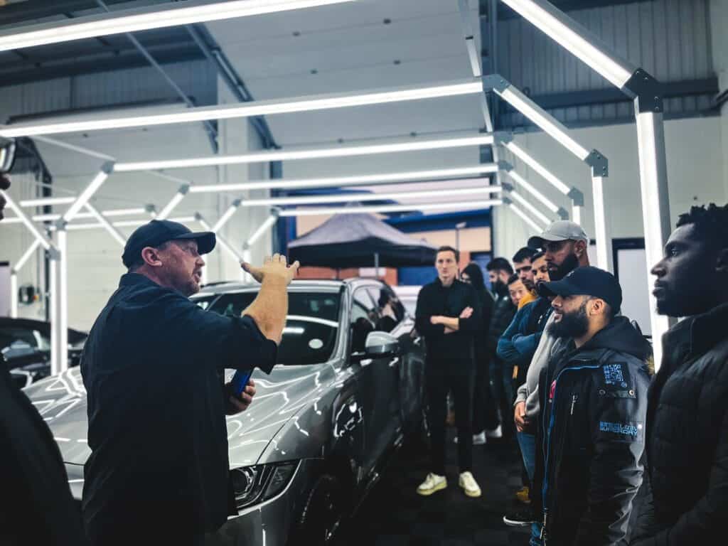 Automotive technician explaining car features to a group in a modern workshop.