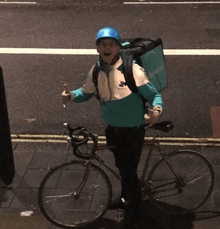 Delivery person with a bicycle and backpack on a city street at night.