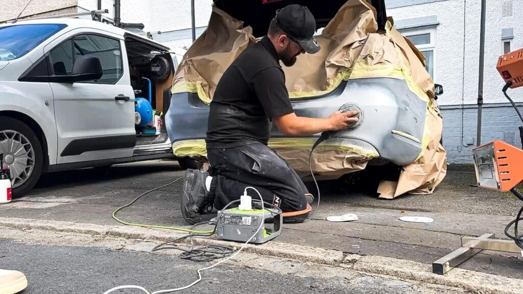 Washdoctors technician sanding a masked bumper on a residential street, with the repair van parked alongside